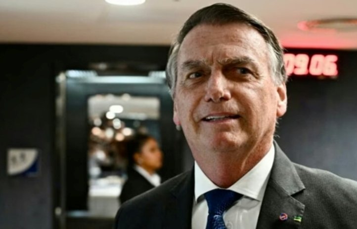 Jair Bolsonaro sonriente en un evento, con fondo oscuro y luces.