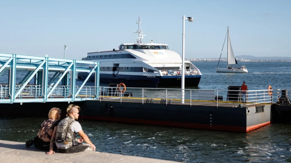 Pareja sentada junto al muelle con barcos en el río Tejo