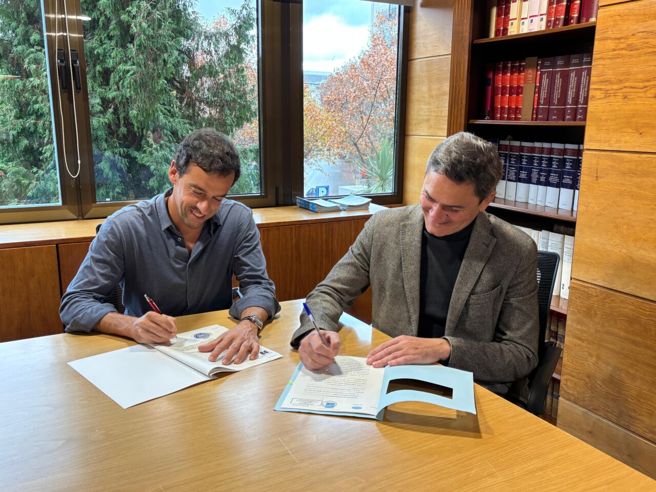 Dos personas firmando un contrato en una mesa de madera.