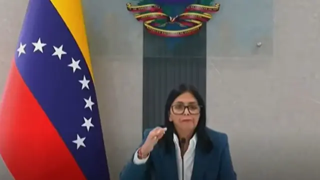 Delcy Rodríguez hablando frente a la bandera de Venezuela