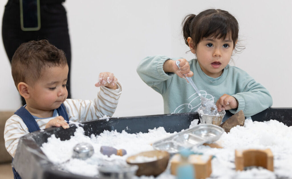 Niños jugando en una mesa con arena blanca y juguetes
