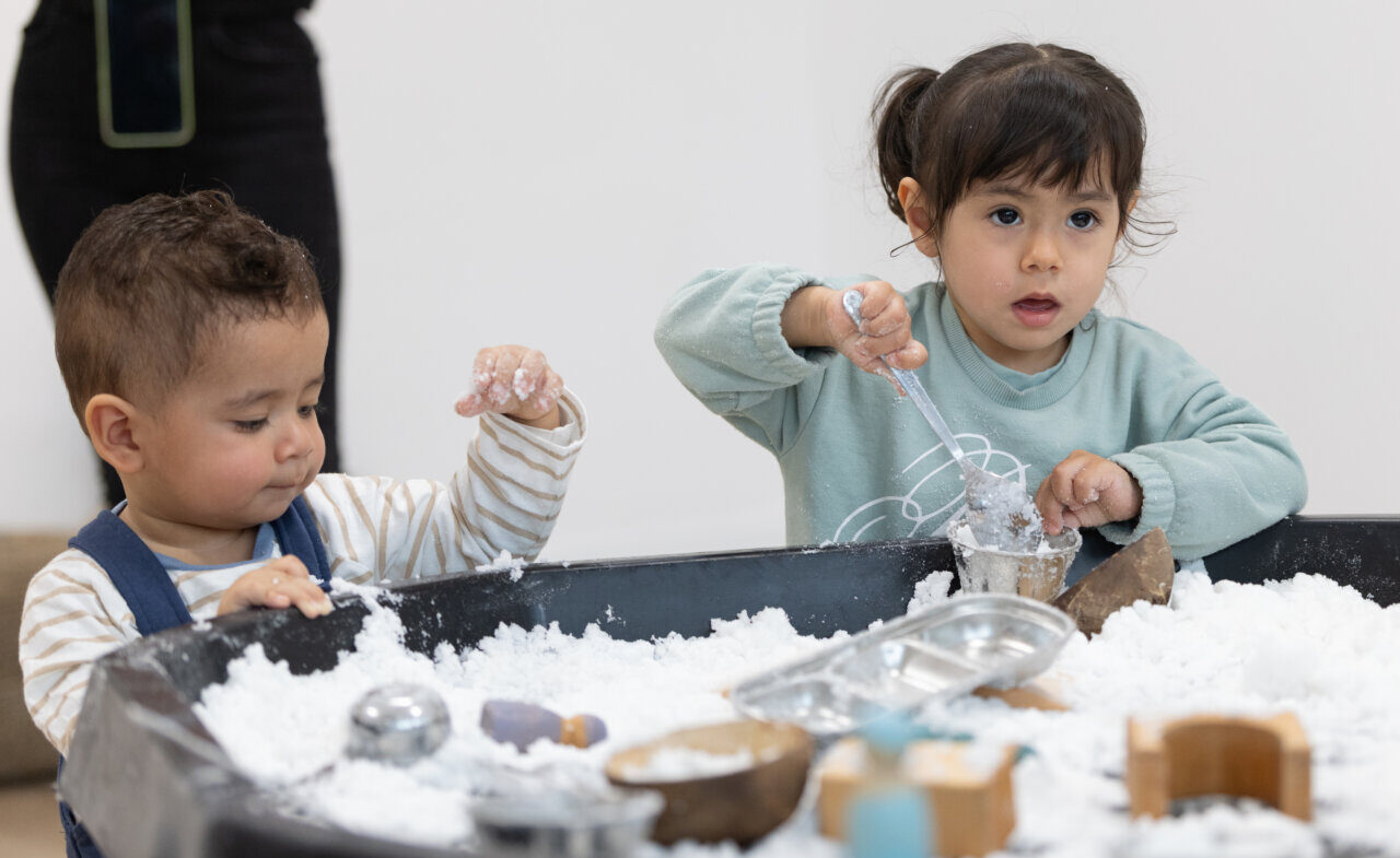 Niños jugando en una mesa con arena blanca y juguetes