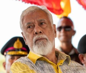 Xanana Gusmão durante um evento, com expressão séria e fundo desfocado.