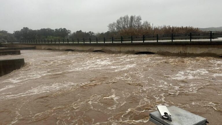 Río crecido con fuerte corriente y puente en el fondo.