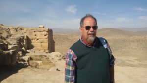 Hombre de pie en un paisaje árido con ruinas antiguas al fondo