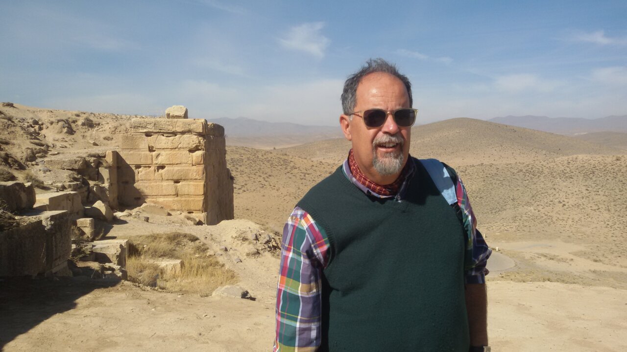 Hombre de pie en un paisaje árido con ruinas antiguas al fondo