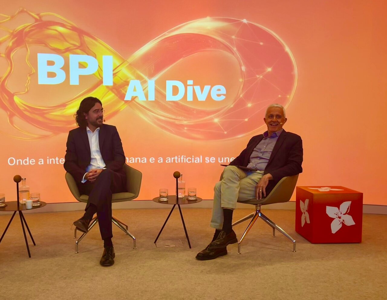 Dos presentadores en el evento BPI AI Dive con fondo naranja
