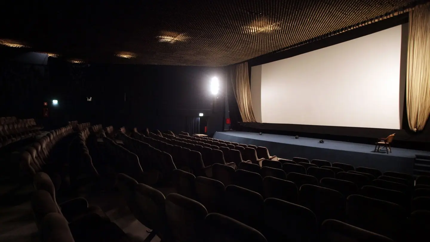 Interior de un cine vacío con una pantalla grande y asientos cómodos