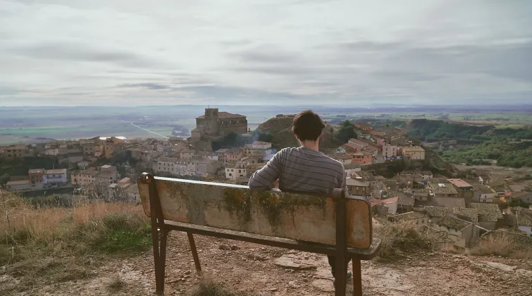 Vista panorámica de un pueblo desde un banco con una persona sentada.