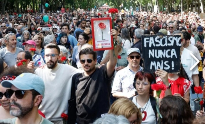 Multitud de personas en una manifestación con carteles y claveles rojos.