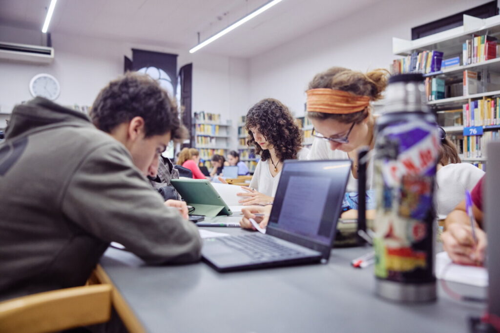 Estudiantes trabajando en una biblioteca, mostrando concentración en sus tareas.
