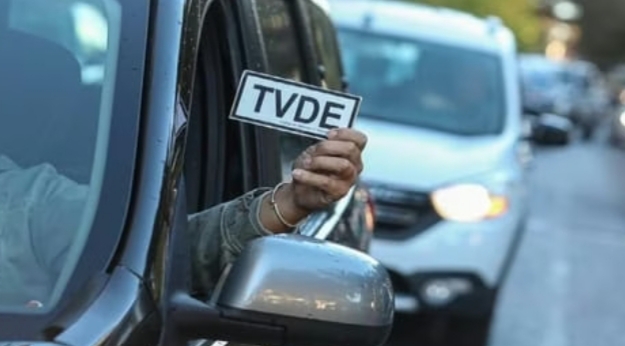 Persona sosteniendo un cartel de TVDE desde un coche en la ciudad.