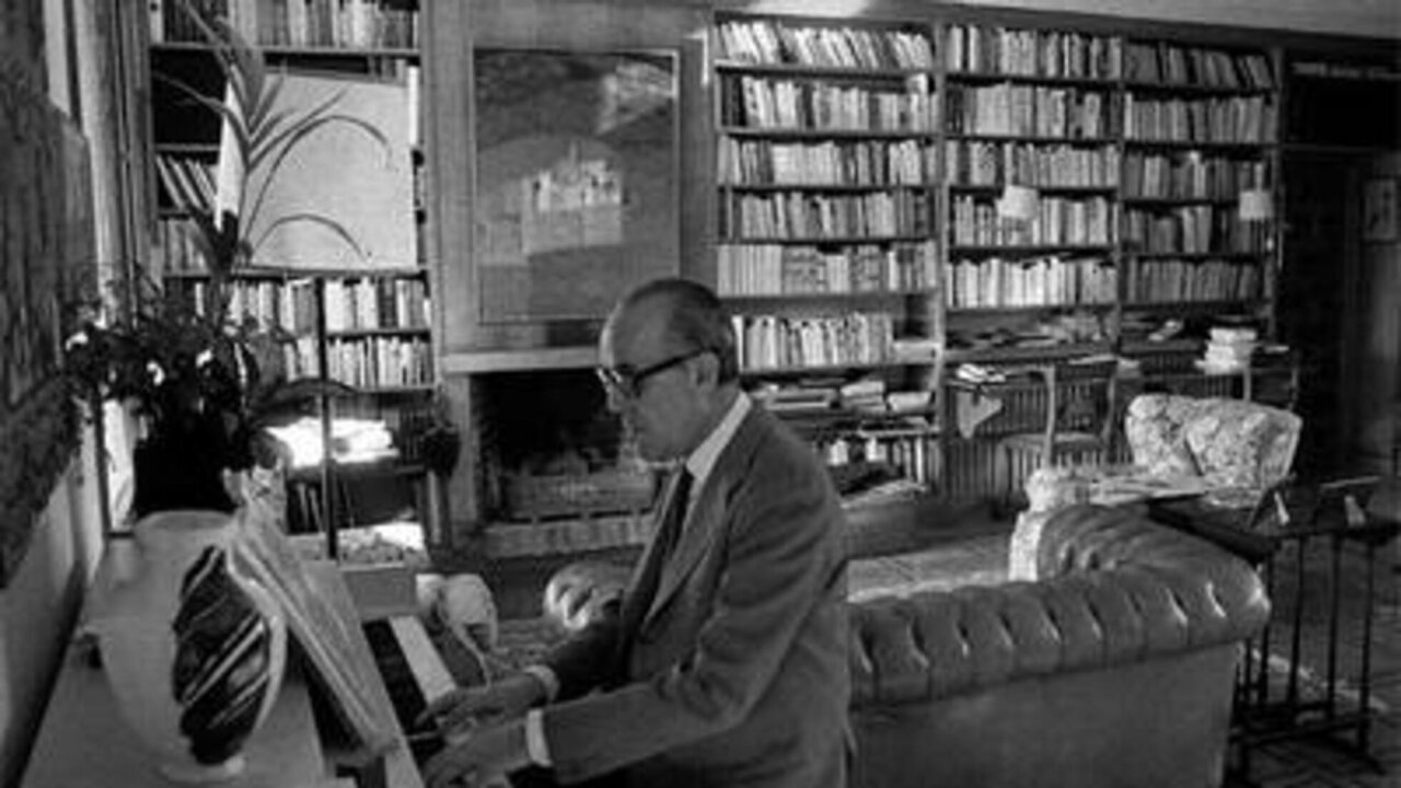 Leopoldo Calvo-Sotelo tocando el piano en un salón con estanterías llenas de libros