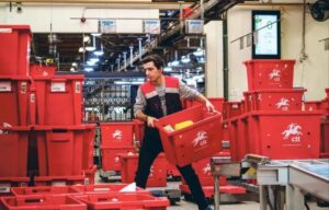 Trabajador de CTT Express manipulando cajas rojas en un centro logístico