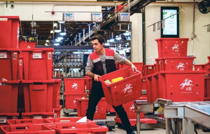 Trabajador de CTT Express manipulando cajas rojas en un centro logístico