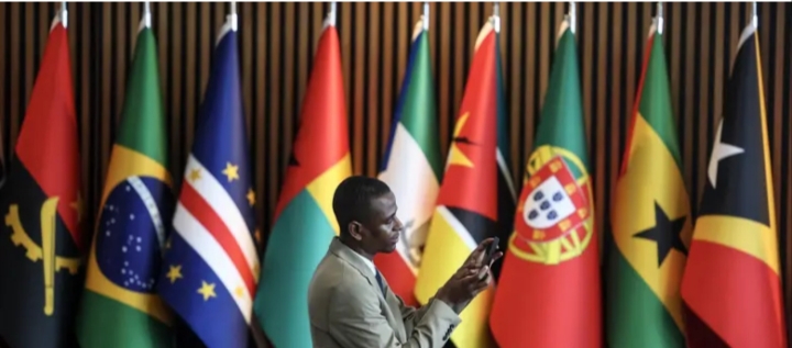 Hombre usando un teléfono móvil frente a banderas de países de la CPLP.