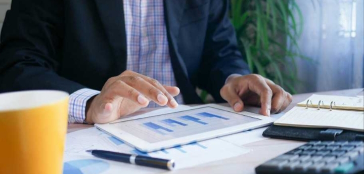 Persona trabajando en una tablet con gráficos y documentos en la mesa