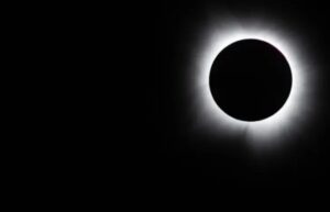 Eclipse total del sol con corona visible en el cielo oscuro.