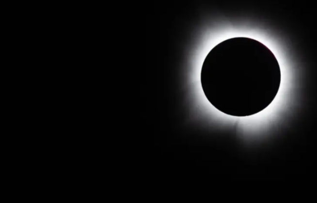 Eclipse total del sol con corona visible en el cielo oscuro.