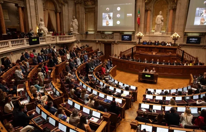 Vista amplia de una cámara parlamentaria con representantes sentados y pantallas encendidas.