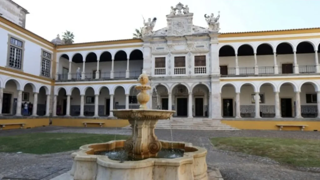 Patio porticado con una fuente de piedra frente a un edificio histórico.
