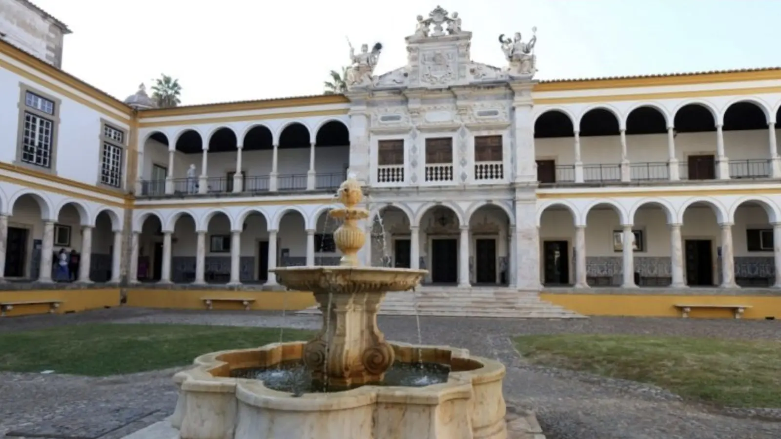 Patio porticado con una fuente de piedra frente a un edificio histórico.
