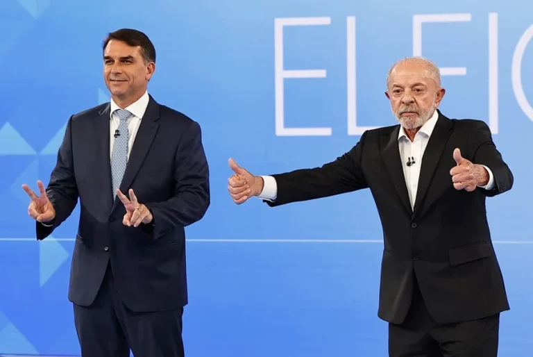 Lula da Silva y Flávio Bolsonaro gesticulan sobre un escenario con fondo azul