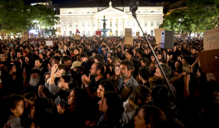 Multitud reunida de noche con pancartas frente a un edificio iluminado