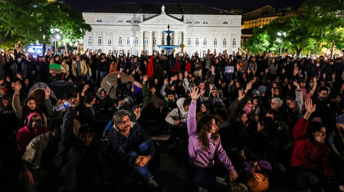 Multitud reunida de noche en una plaza frente a un edificio iluminado.