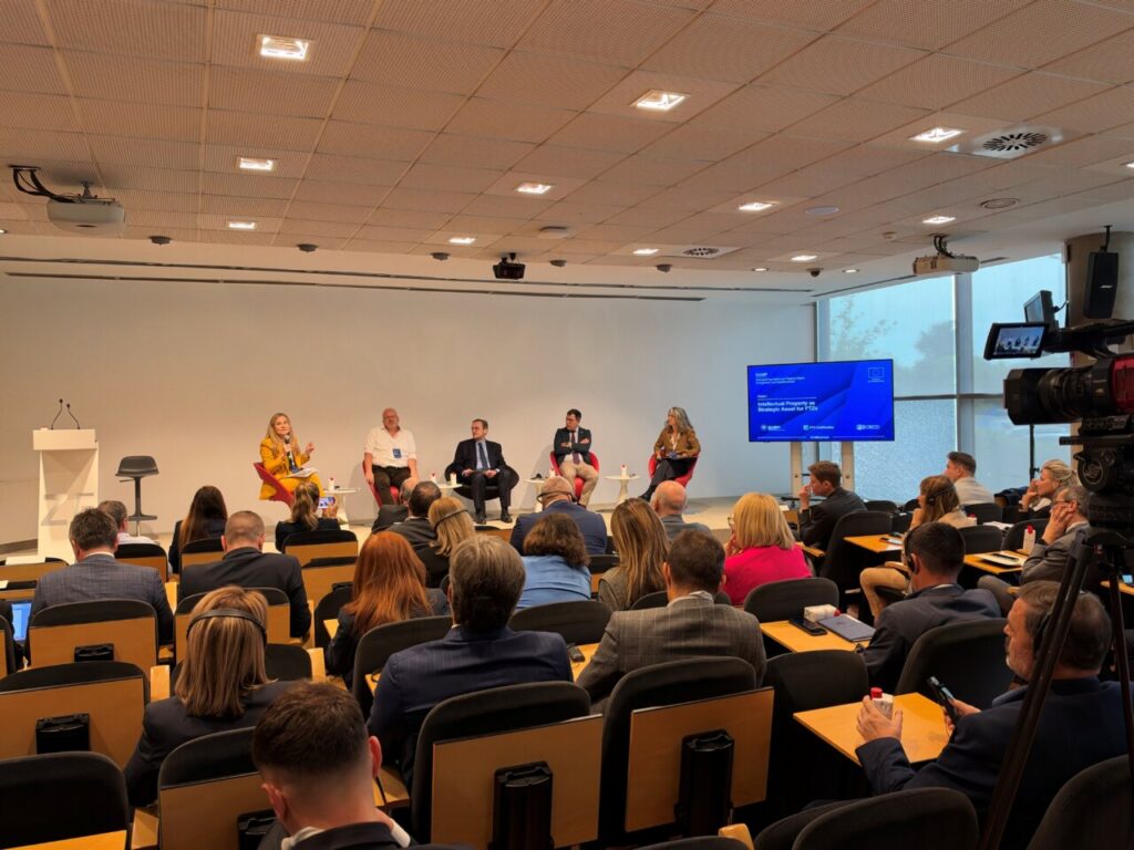 Panelistas hablan ante un público sentado en una sala de conferencias.