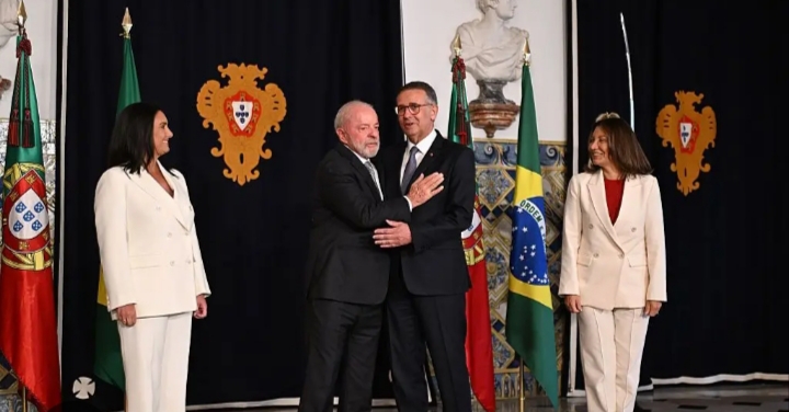 Cuatro personas posan frente a las banderas de Portugal y Brasil.
