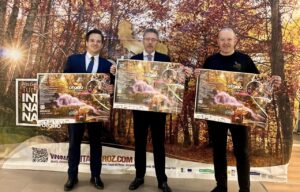 Tres hombres sostienen carteles del Otoño Mágico ante un fondo de bosque otoñal.