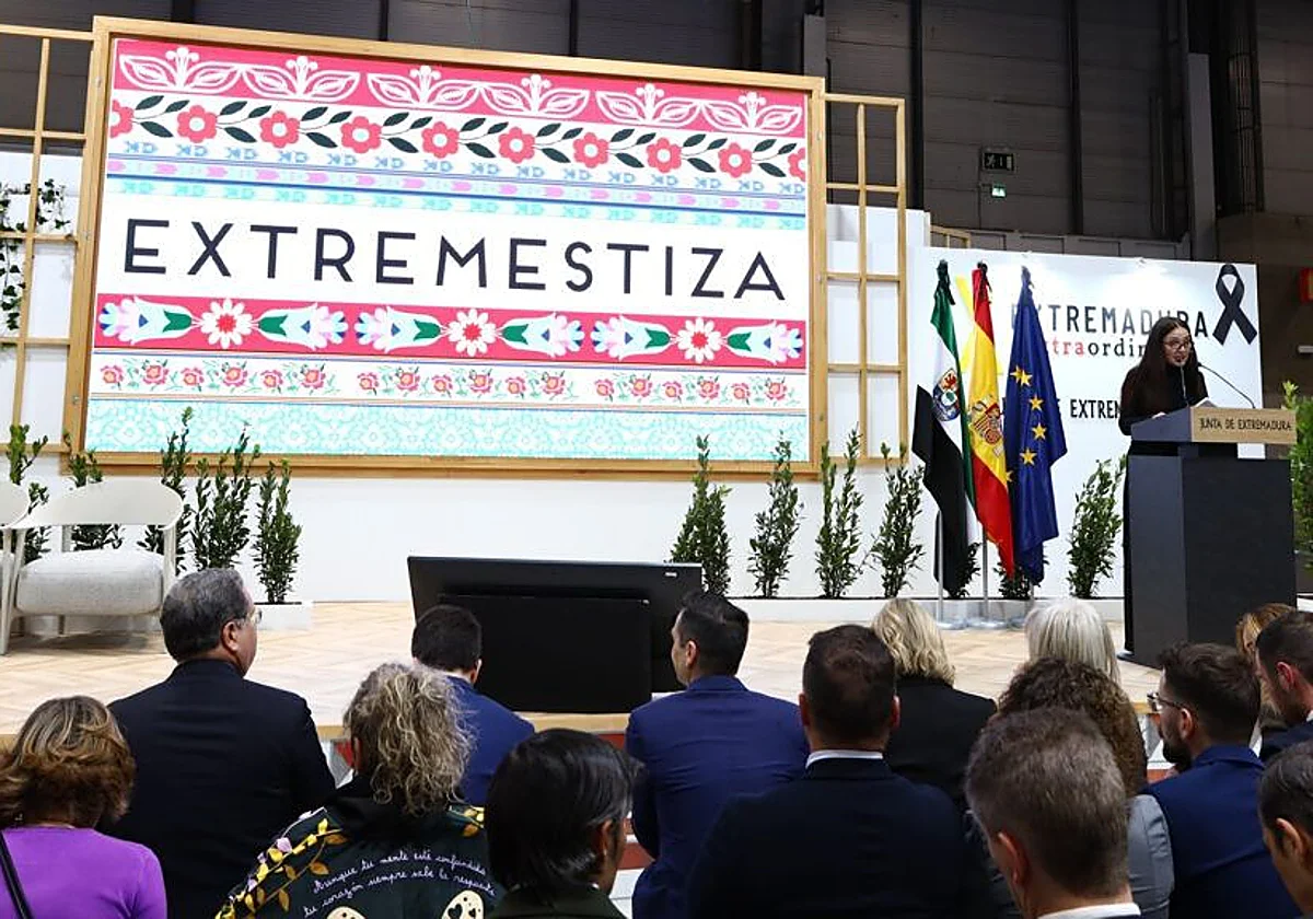Una mujer habla en un atril ante el público, bajo un rótulo de Extremestiza.
