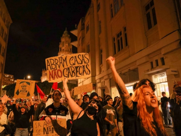 Manifestantes protestan de noche con pancartas sobre vivienda y puños en alto
