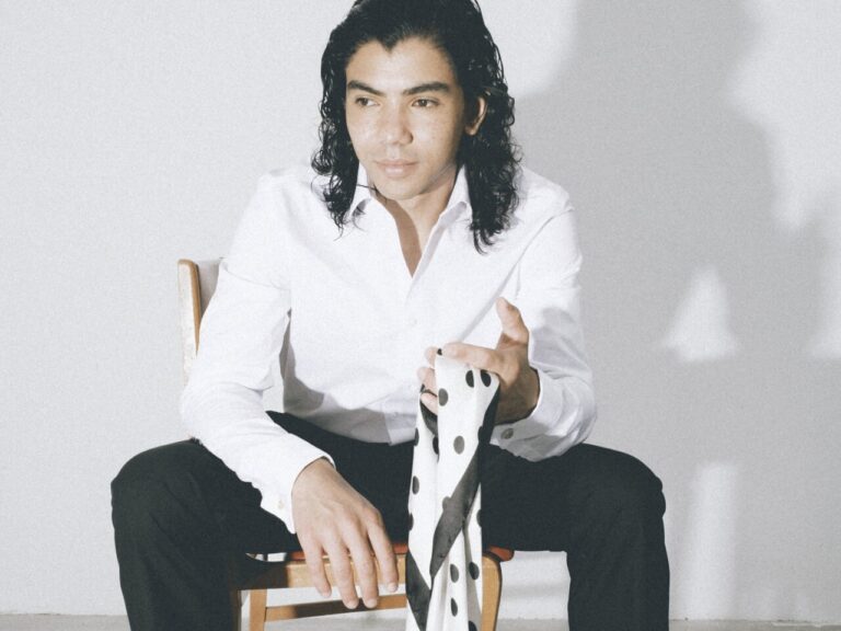 Hombre sentado con camisa blanca sostiene una tela blanca con manchas negras