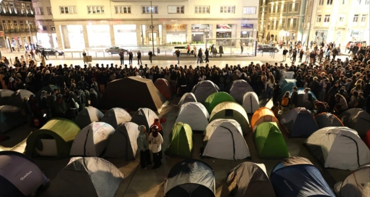 Numerosas tiendas de campaña y personas ocupan una plaza iluminada durante la noche.
